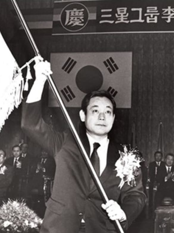 A black-and-white photo of Chairman Lee Kun-hee waving a Samsung flag at his inauguration as Chairman in December 1987.