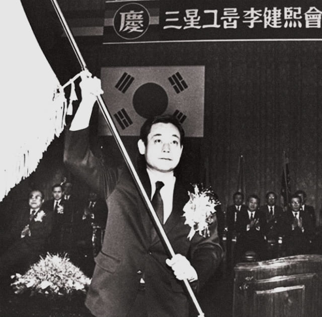 A black-and-white photo of Chairman Lee Kun-hee waving a Samsung flag at his inauguration as Chairman in December 1987.