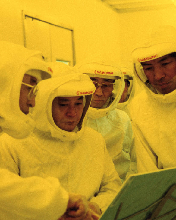A photo of Chairman Lee Kun-hee inspecting a semiconductor production line in a dust-proof suit while listening to staff explanations.