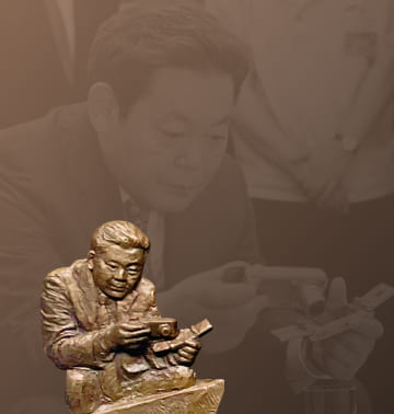 A photo and relief of Chairman Lee Kun-hee inspecting digital cameras and mobile phones at the 2003 Advanced Products Exhibition.